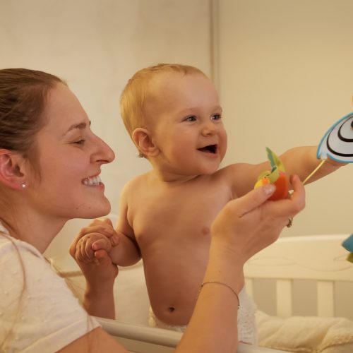 Portrait of smiling baby with mother playing with spinning toys hanging on mobile in bed at night